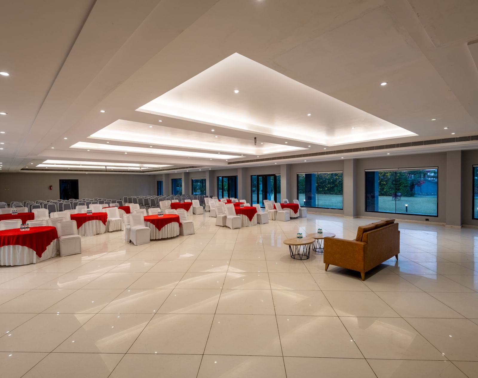 Side view of tables with neatly decorated tablecloths, a plush sofa, and two round tables set in front at DLS Forest Vines Resort | Wedding Venues in Jim Corbett